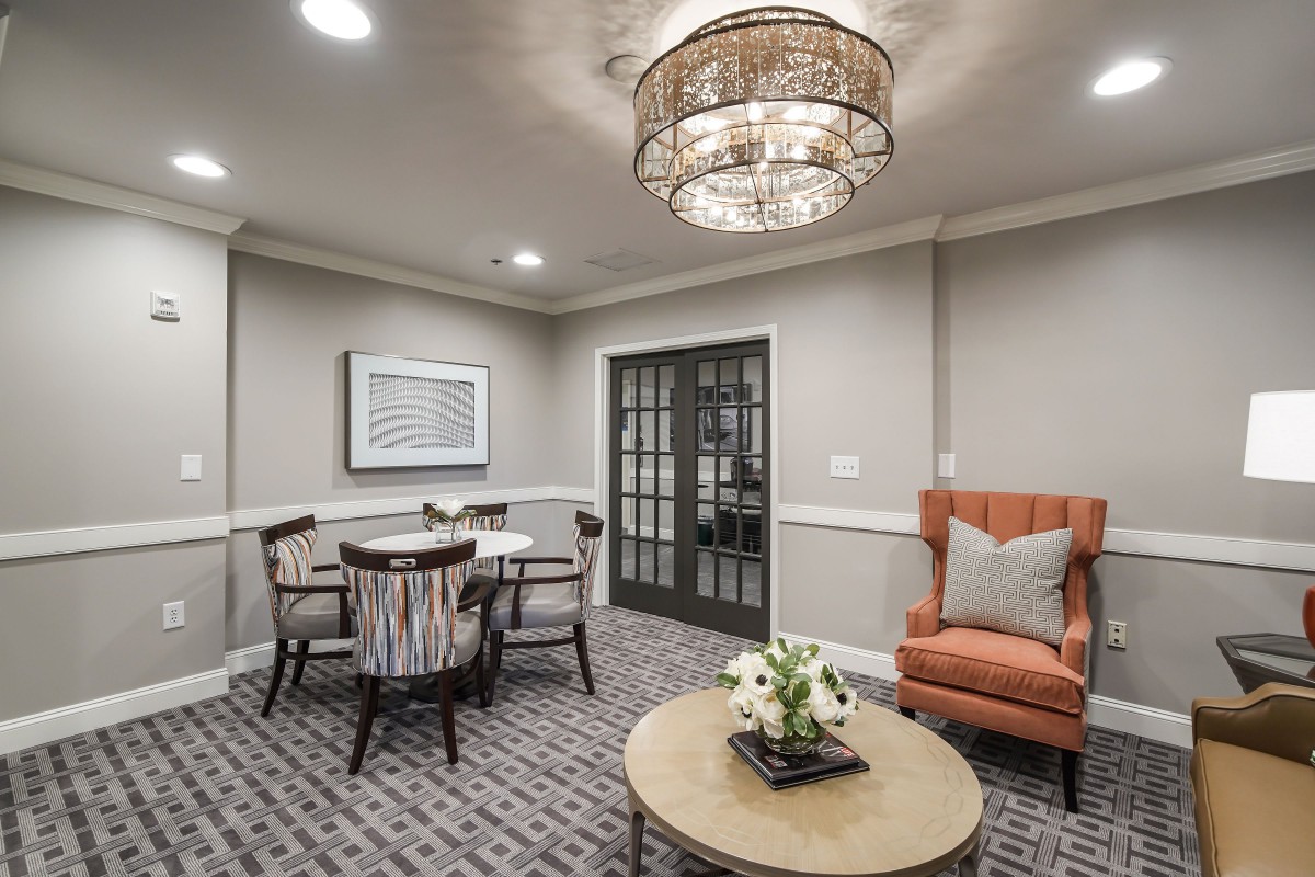 A cozy living room with elegant dcor, featuring a round coffee table, an armchair, and a dining set under a stylish chandelier.