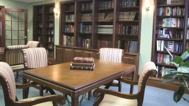 A cozy library with a wooden table surrounded by bookshelves and chairs.