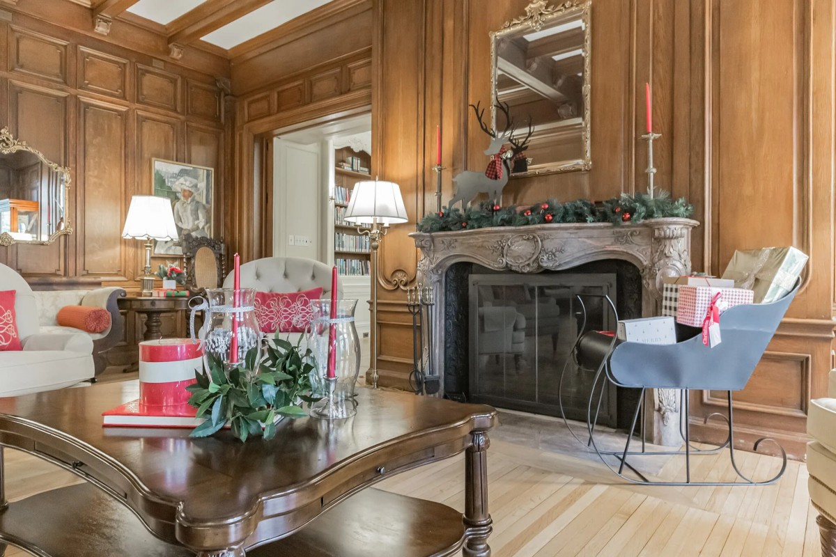 A cozy living room featuring wood paneling and a decorated fireplace, adorned with holiday decorations and elegant furnishings.