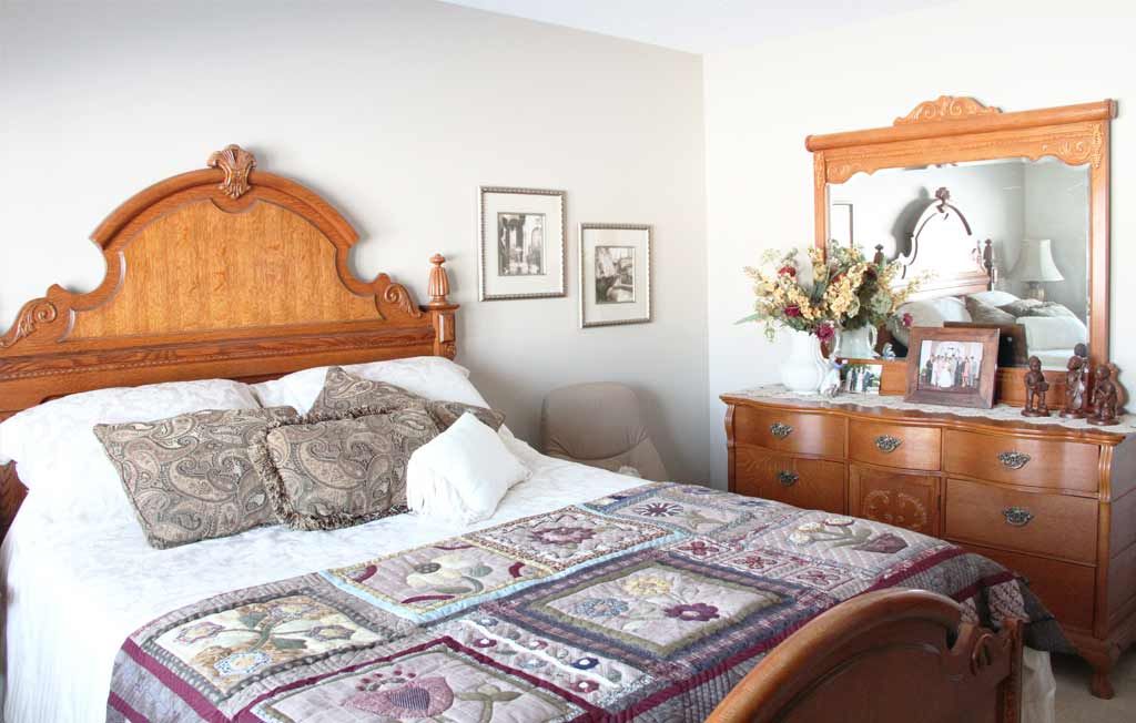 A cozy bedroom featuring a wooden bed with a quilt, accompanied by a matching dresser with a mirror and decorative touches.
