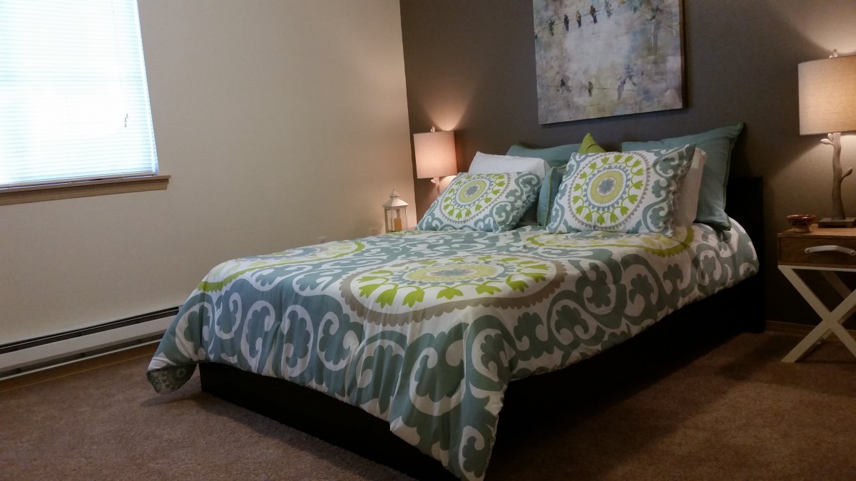 A cozy bedroom with a patterned bedspread and a bedside lamp.