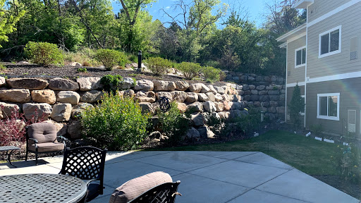 A peaceful outdoor garden scene featuring a rocky wall, lush greenery, and a patio area.