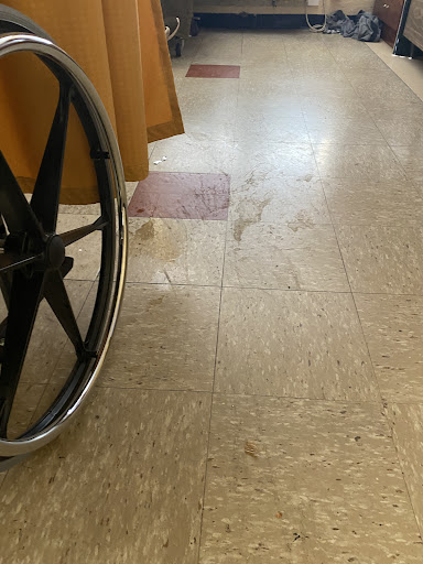 A close-up view of a wheelchair positioned next to a polished floor, possibly in a healthcare setting.