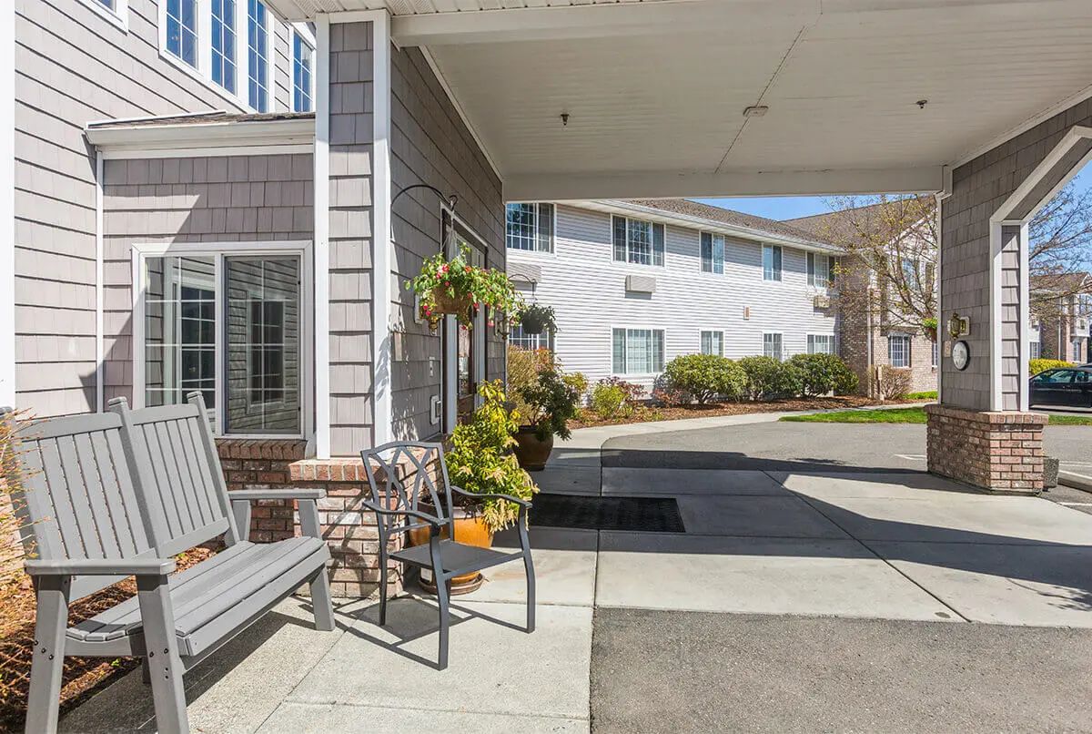 A welcoming entrance of a residential building with benches and plants under a covered walkway.