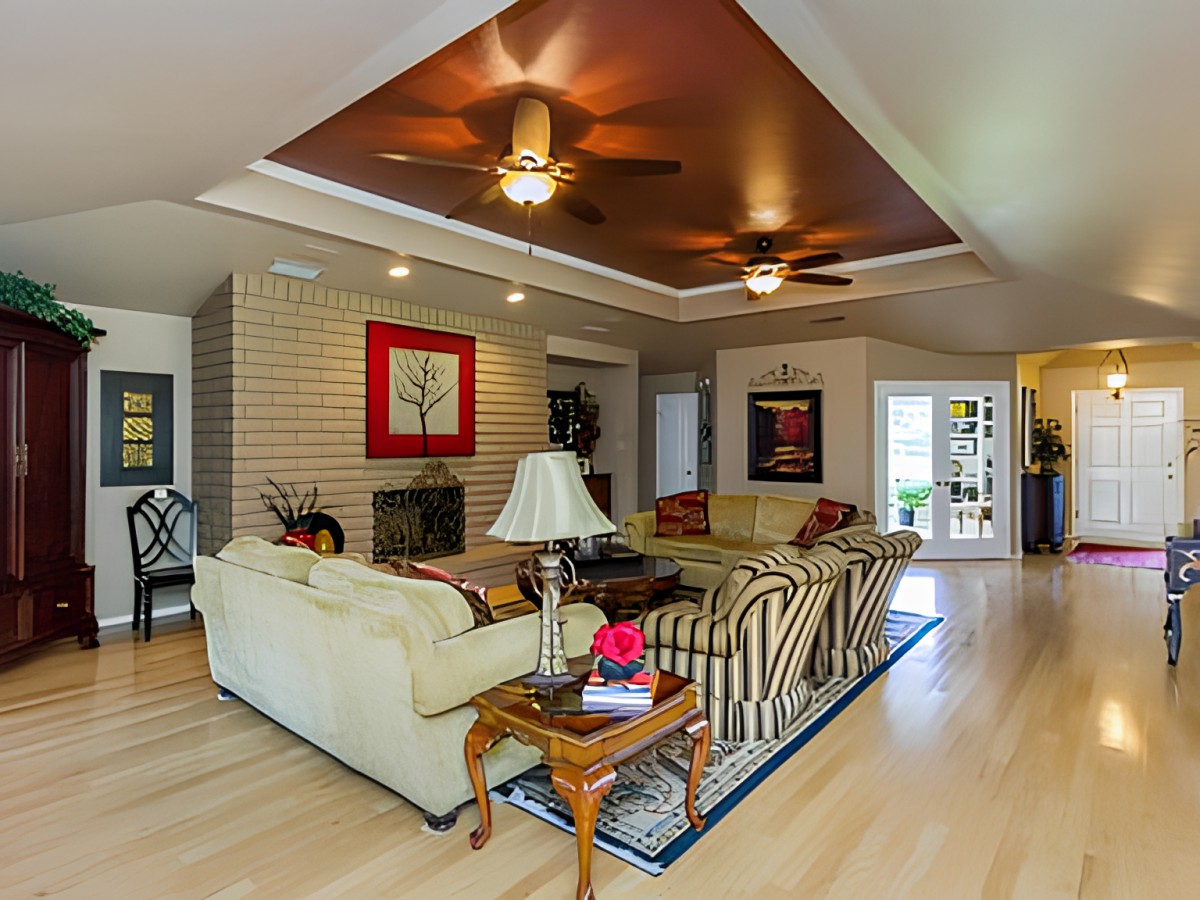 A spacious and well-lit living room featuring cozy sofas, a coffee table, ceiling fans, and artwork on the walls.