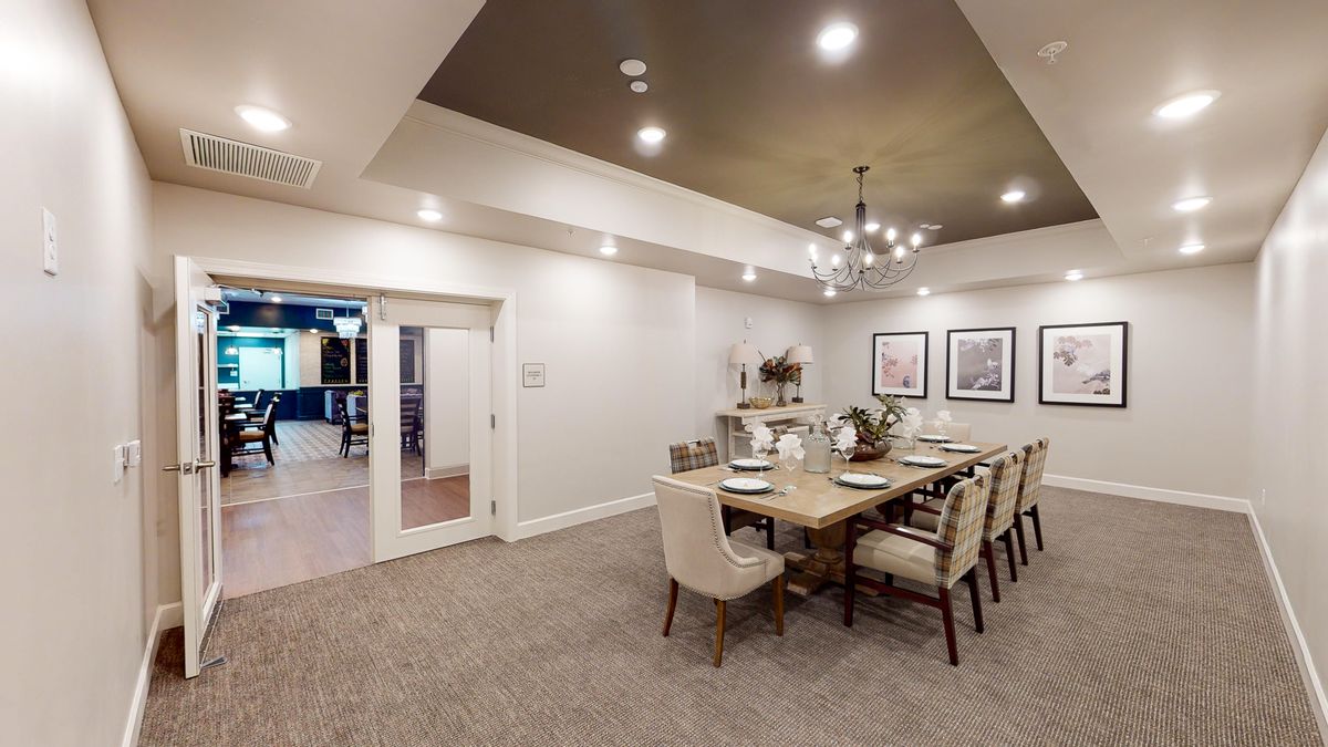 A spacious dining room with elegant decor, featuring a large table set for dining under a stylish chandelier.
