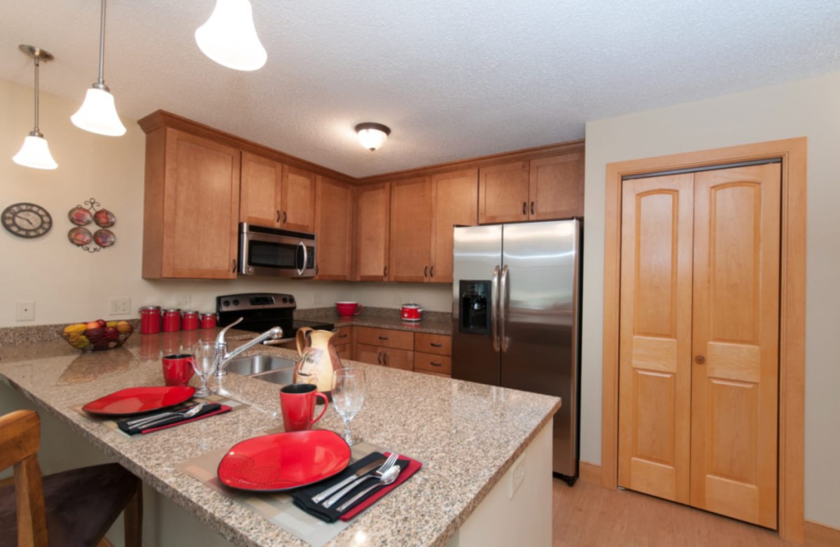 A modern kitchen featuring wood cabinets and stainless steel appliances, complemented by a granite countertop and red accent decor.