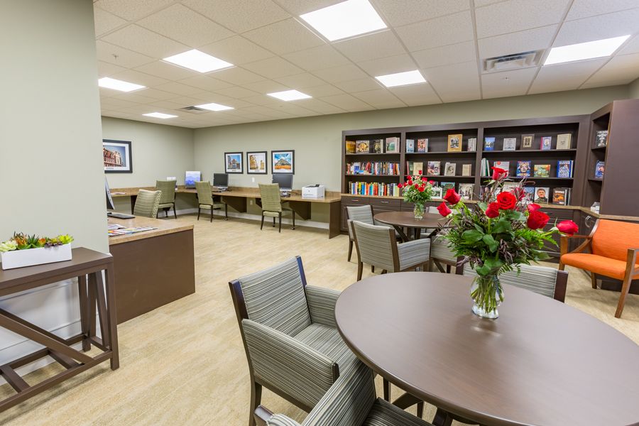 A cozy library reading room with tables, chairs, bookshelves, and computers.