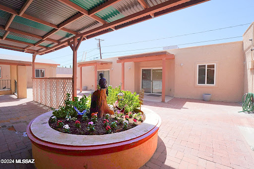 A serene courtyard featuring vibrant flowers and a decorative sculpture, surrounded by residential buildings.