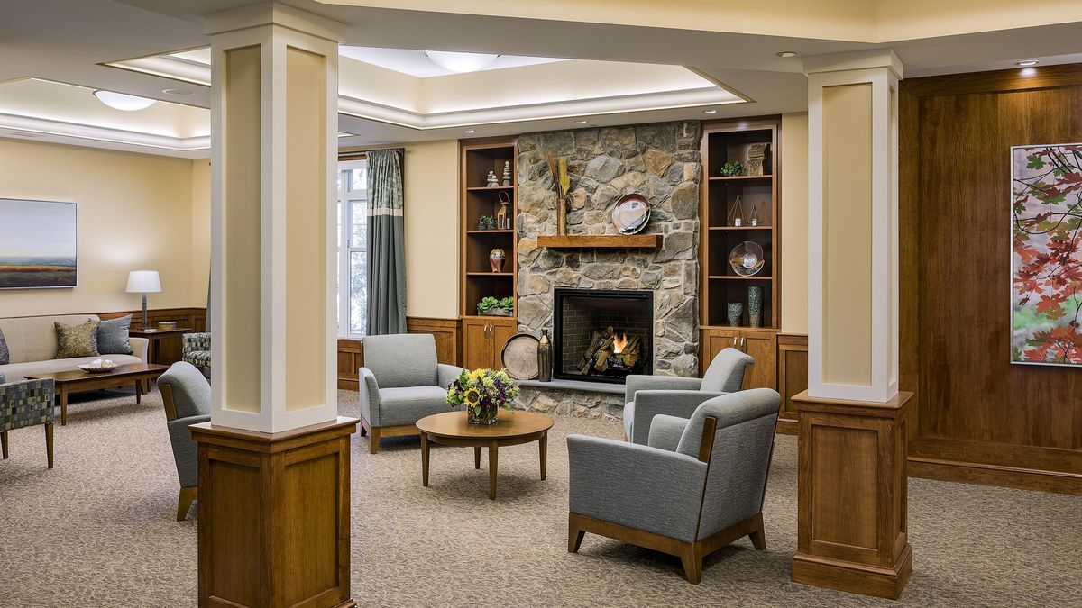 A cozy living room with a stone fireplace, surrounded by comfortable armchairs and wooden shelves.