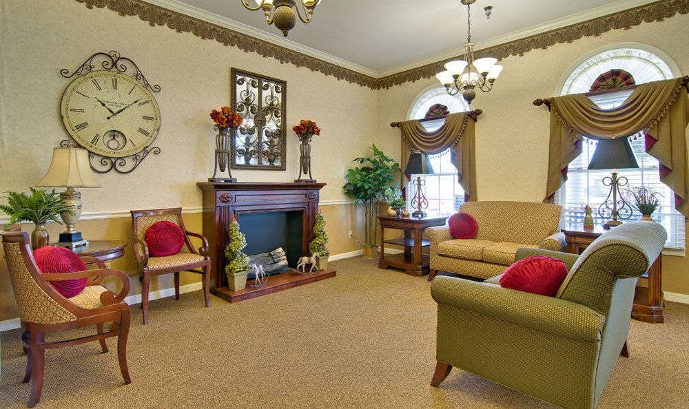 A traditionally styled living room with a fireplace, armchairs, and sofas adorned with red cushions.