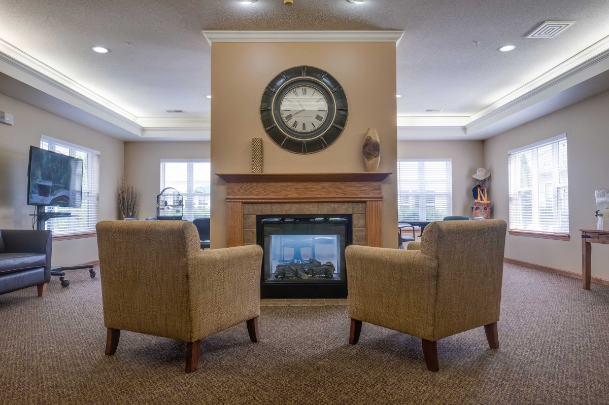 A cozy living room featuring two chairs facing a modern fireplace with a large clock above it.