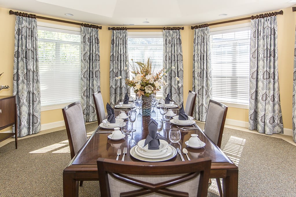 An elegantly set dining room table with a floral centerpiece and patterned curtains.