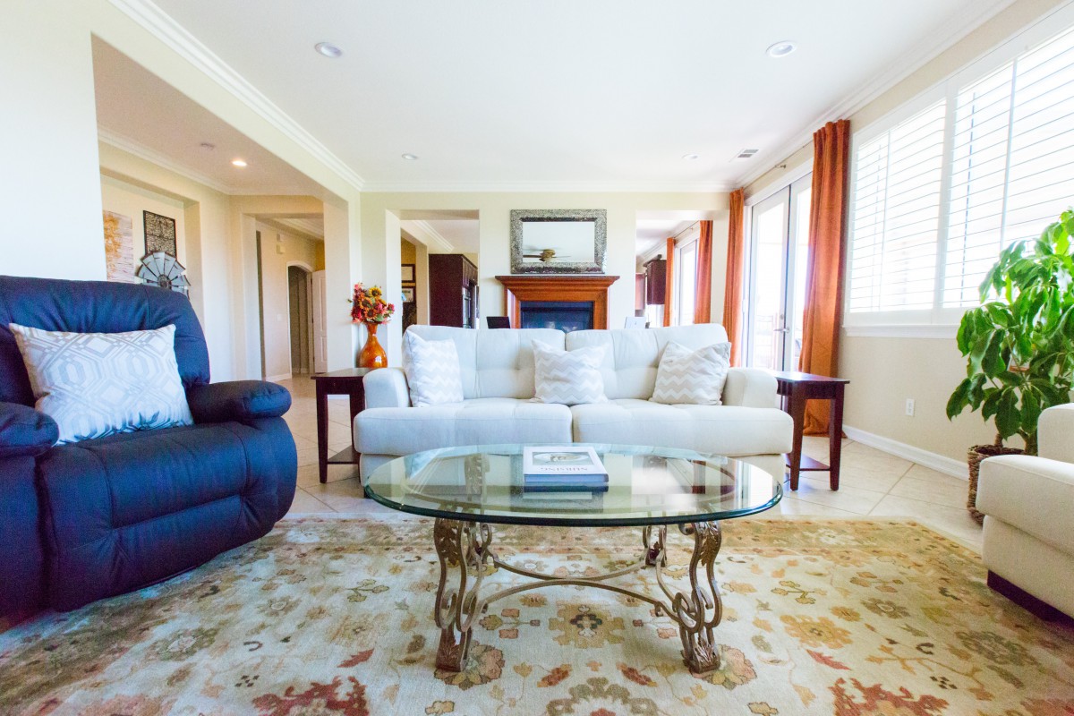 A bright and spacious living room featuring a white sofa, a glass coffee table, and a patterned rug.