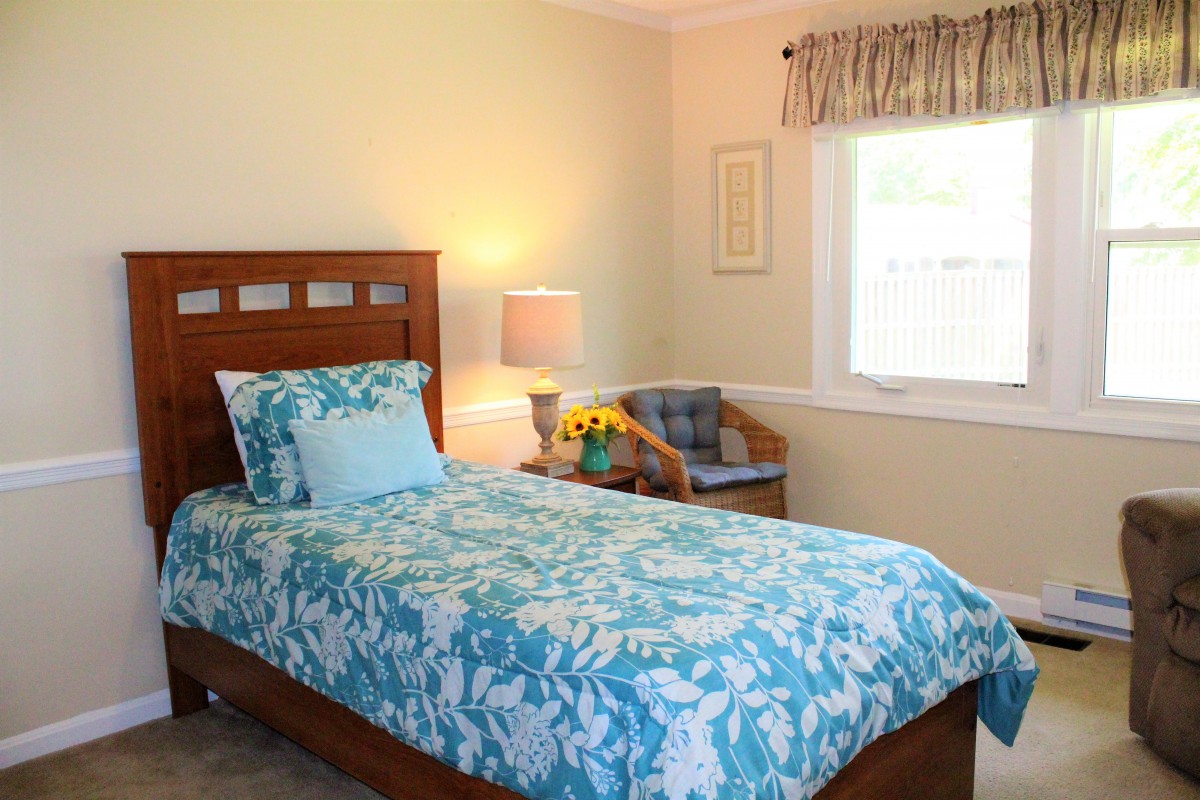 Cozy bedroom with a single bed and floral bedding, featuring a lamp and chair by the window.