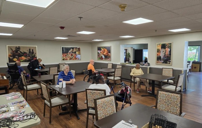 A group of elderly people sitting in a dining hall, engaging in conversation.