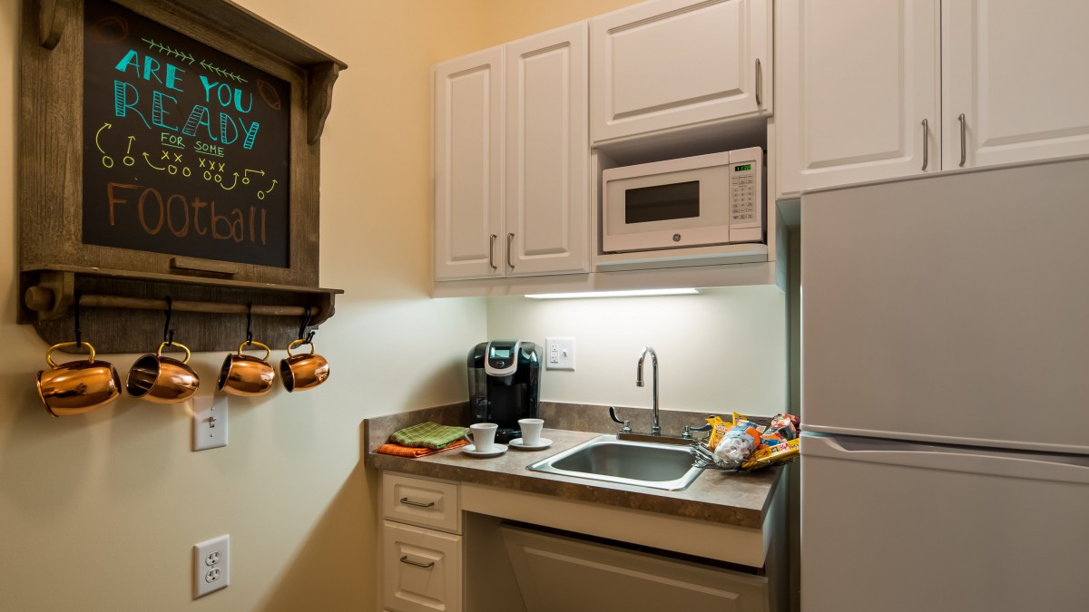 A compact kitchen with a microwave, sink, coffee maker, and overhead cabinets.