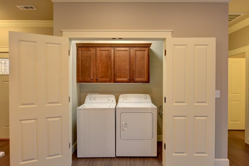 A compact laundry area with a washing machine and dryer, enclosed by double doors, featuring overhead cabinets for storage.