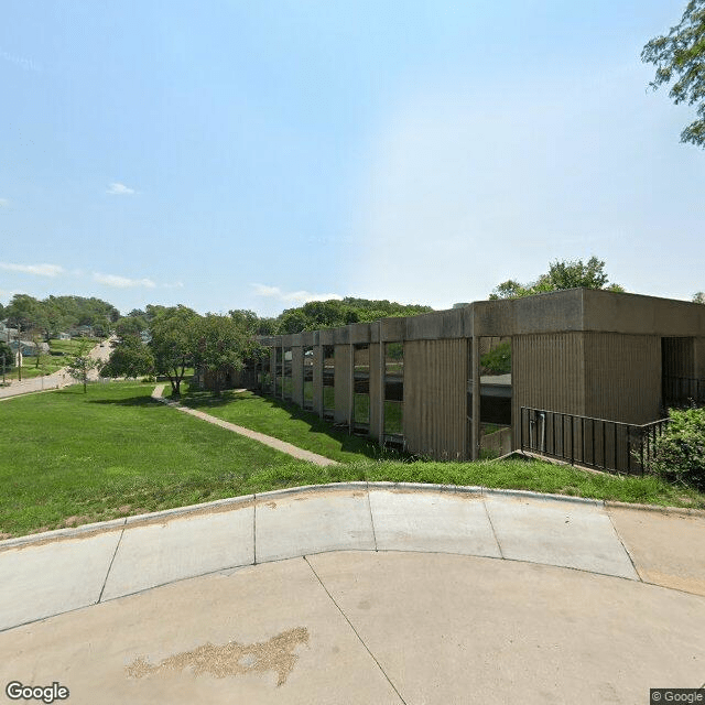 A suburban apartment building surrounded by green space and pathways on a sunny day.