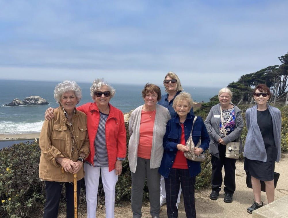 A group of older adults posing for a photo with the ocean in the background.