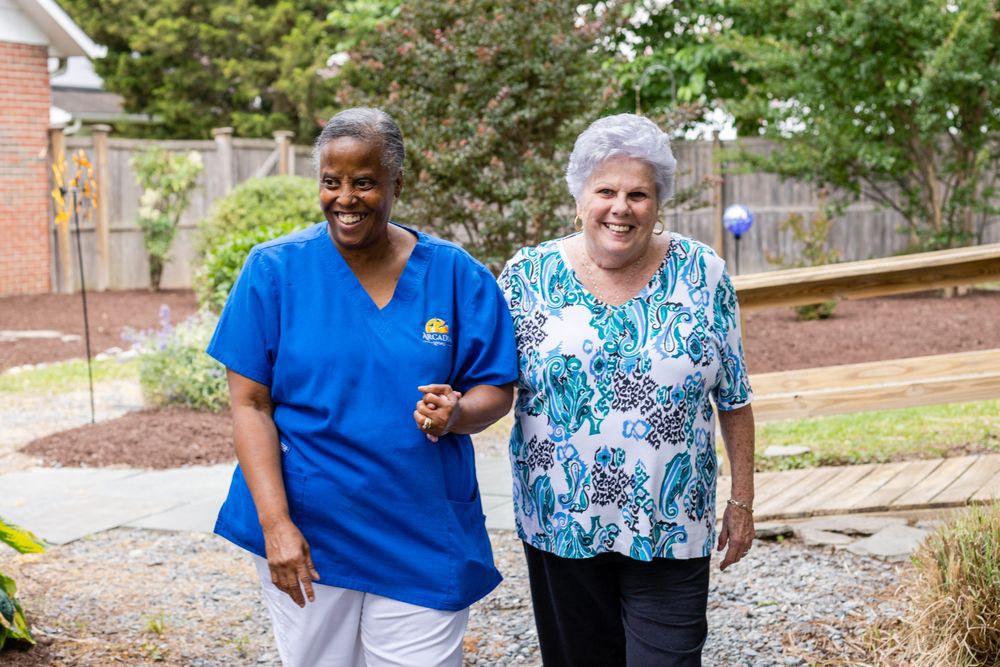 A healthcare worker walking with a senior woman outdoors, providing companionship and support.