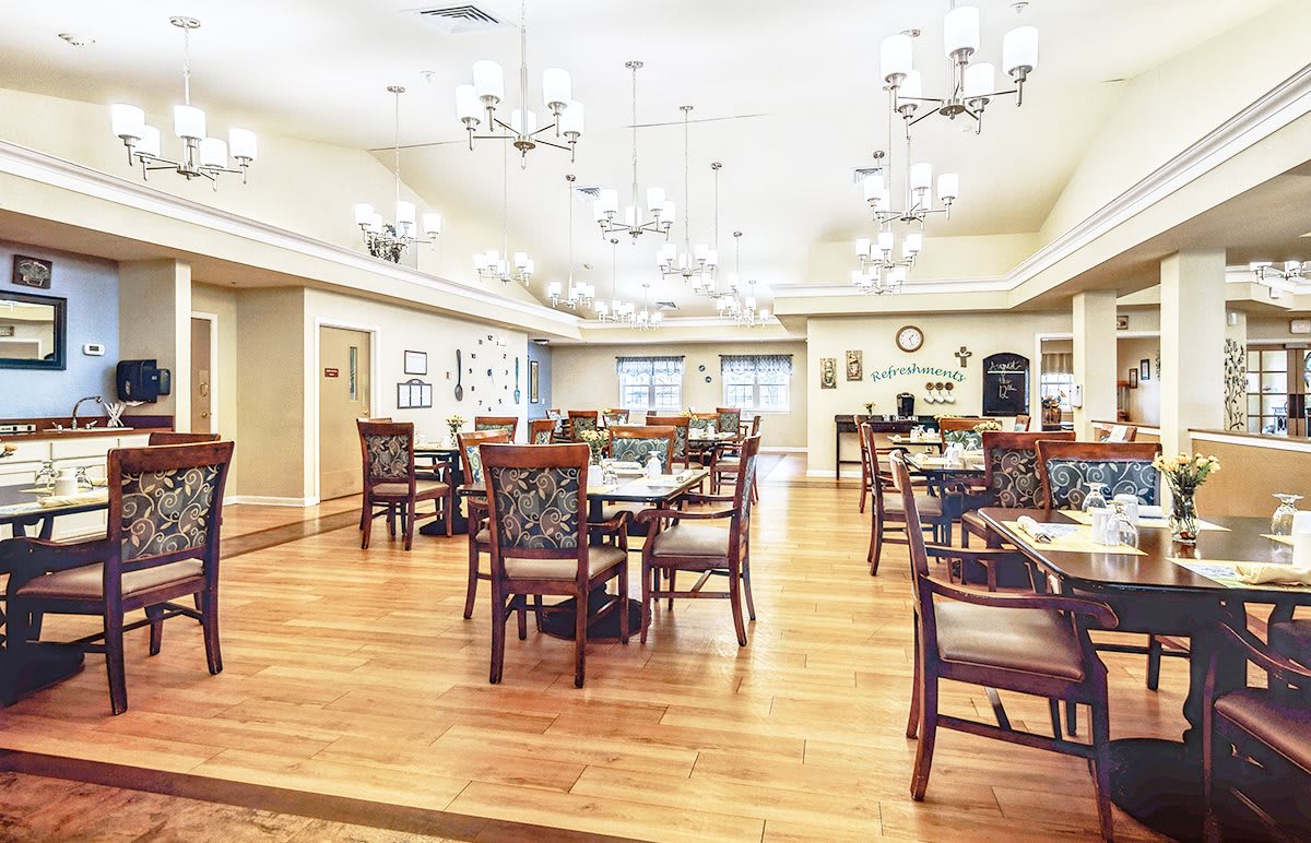A spacious dining area with elegant chandeliers, wooden floors, and neatly arranged tables and chairs.