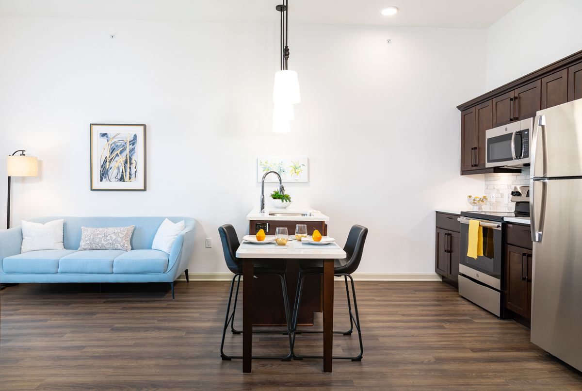 A modern kitchen and dining area featuring an island counter with bar stools, laminate flooring, and a cozy couch.