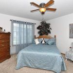 A cozy bedroom with a blue bedspread, wooden dresser, and ceiling fan.