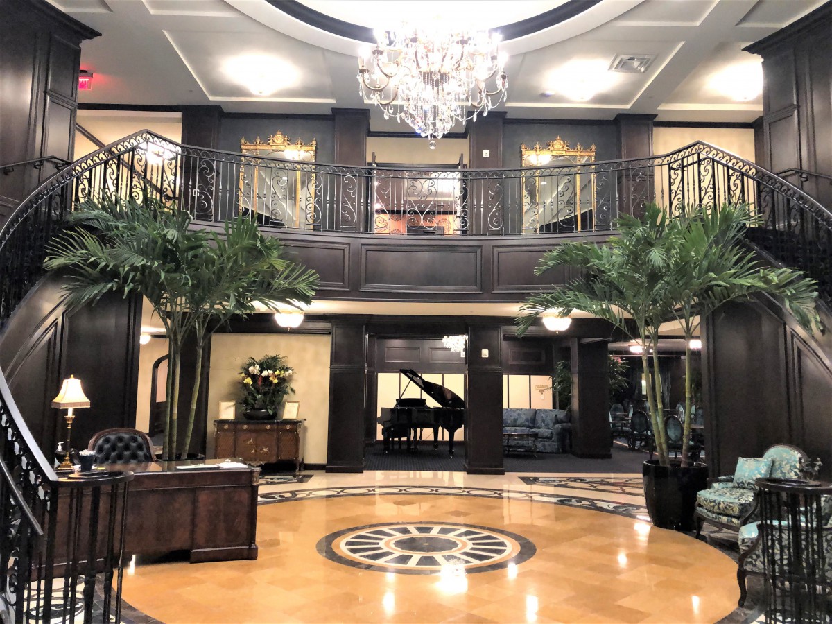 A luxurious hotel lobby featuring a grand chandelier, elegant architecture, and a grand piano.