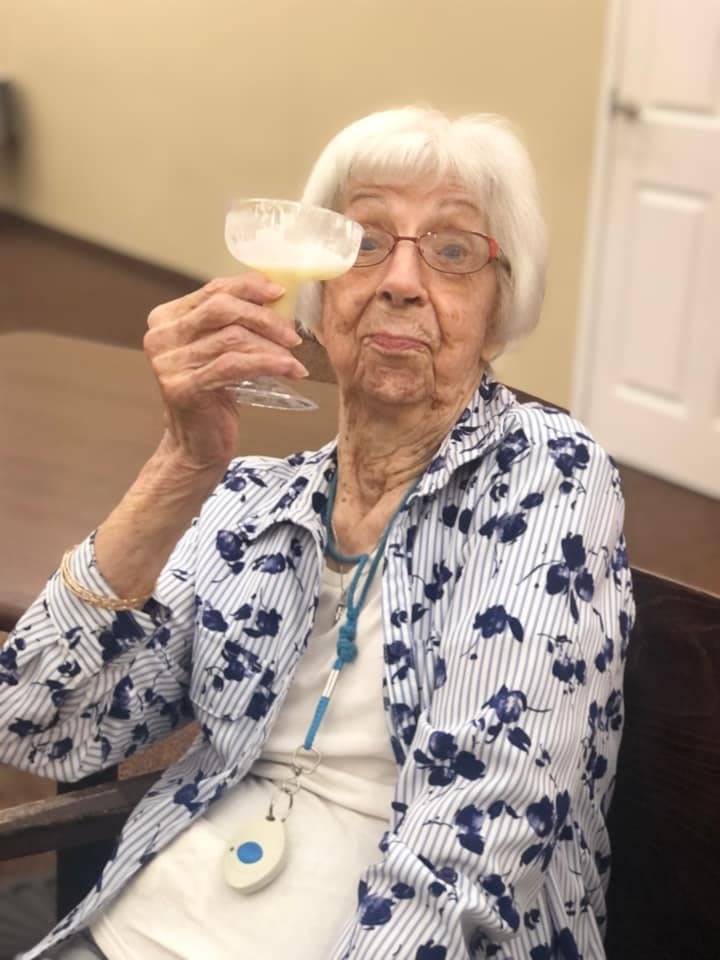 An elderly woman enjoying a drink, raising her glass in celebration.