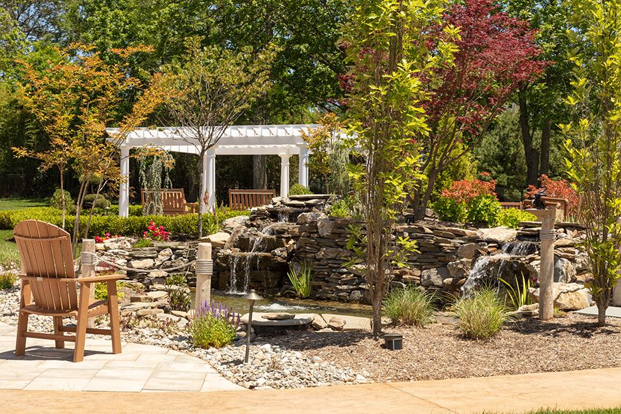 A serene garden featuring a waterfall, pergola, and outdoor seating surrounded by lush trees.