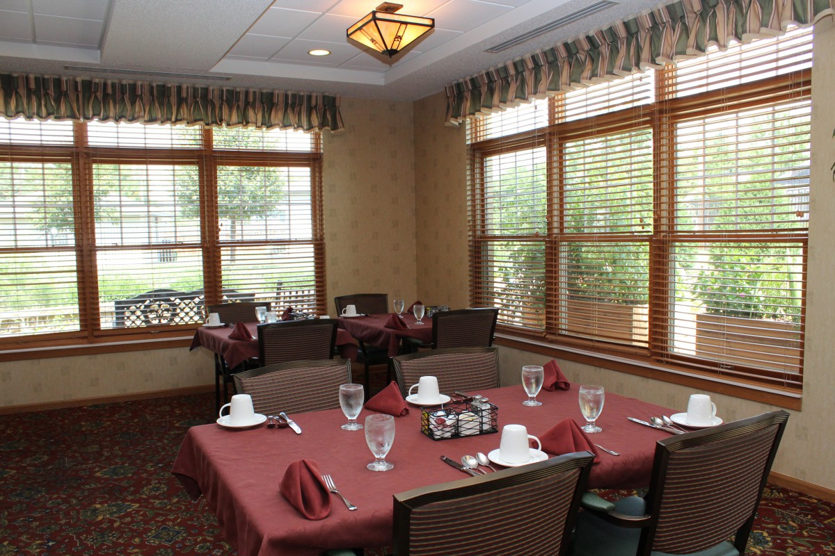 A cozy dining room with elegantly set tables, featuring red tablecloths and neatly arranged glassware.