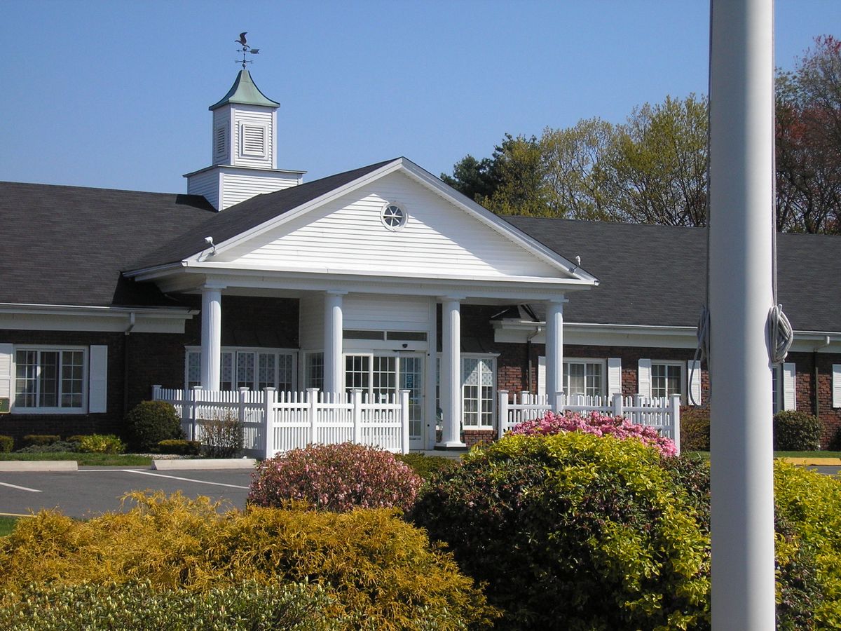 A well-manicured entrance to a building with white columns and surrounding landscaping.