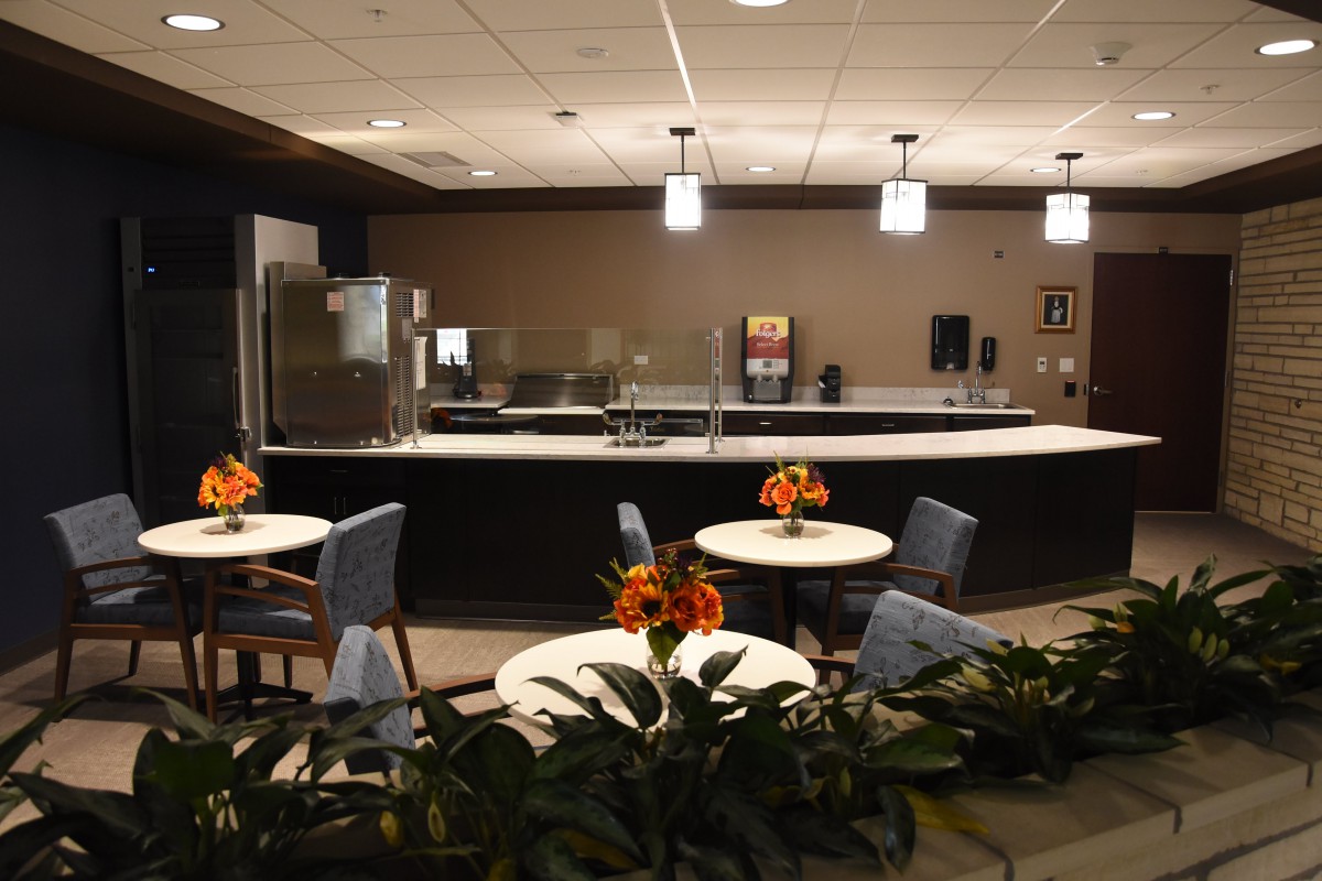 A modern cafe interior with tables and chairs, decorated with plants and floral arrangements.