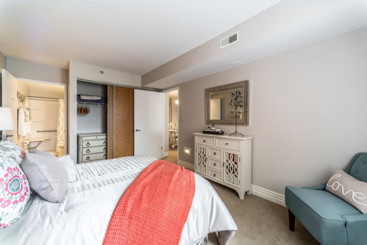 A cozy bedroom featuring a neatly made bed with a red throw, an open closet, and a decorative dresser with a mirror above it.