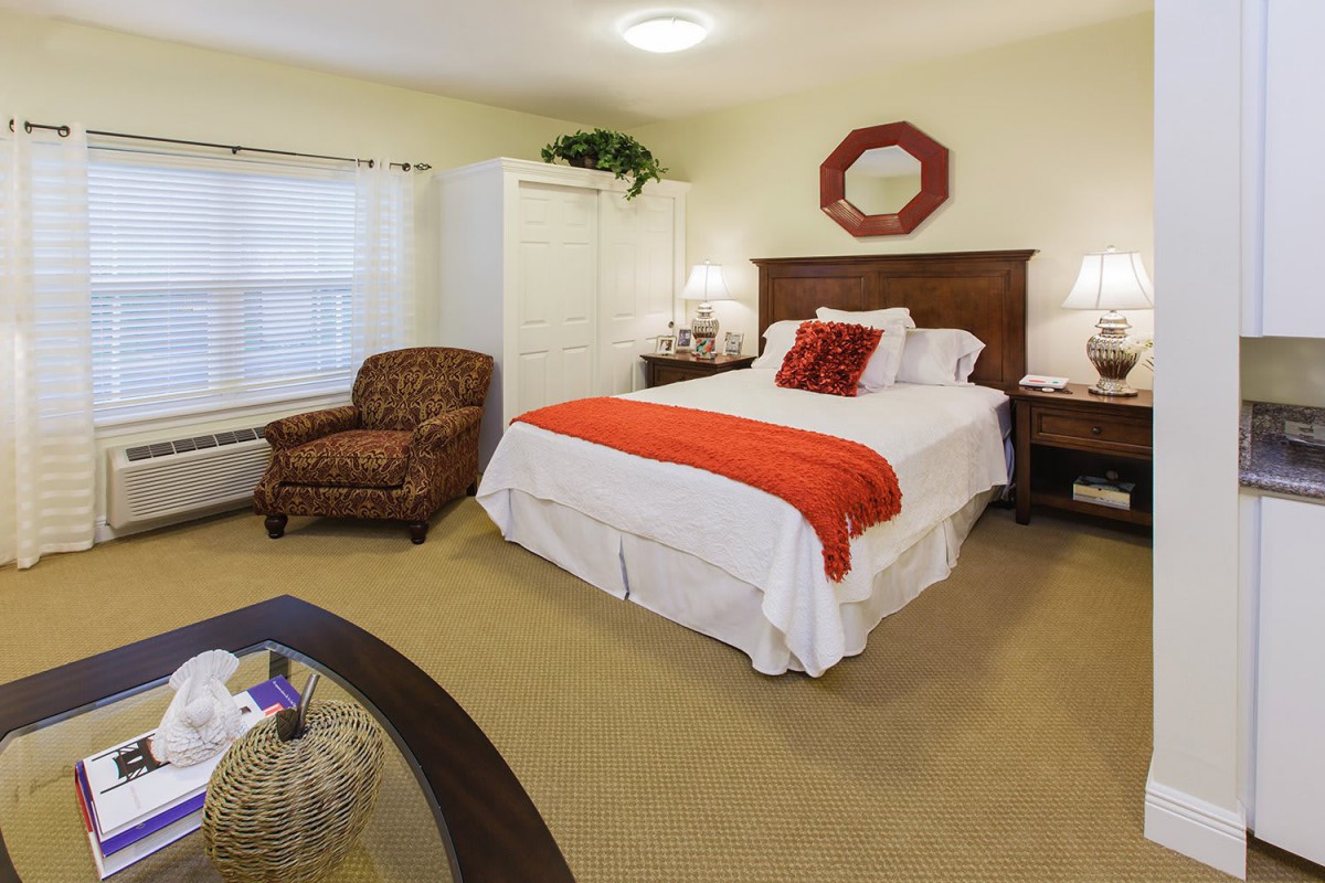 A cozy bedroom with a neatly made bed, armchair, and warm lighting.