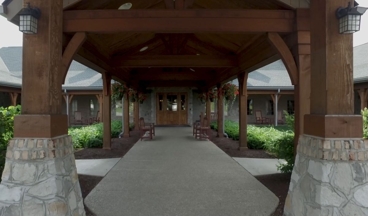 A wooden entrance pathway leading to a building, surrounded by gardens.