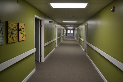 A long indoor corridor with green walls and multiple doors.