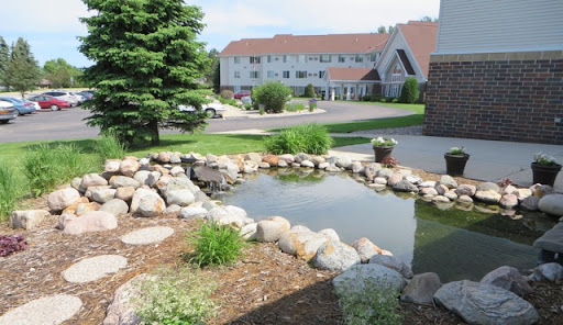 A serene pond surrounded by rocks and greenery, with a hotel in the background.