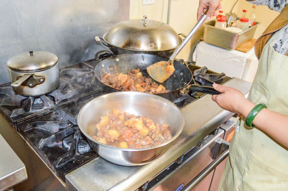 Person cooking food in a kitchen using multiple pots and pans on a stove.