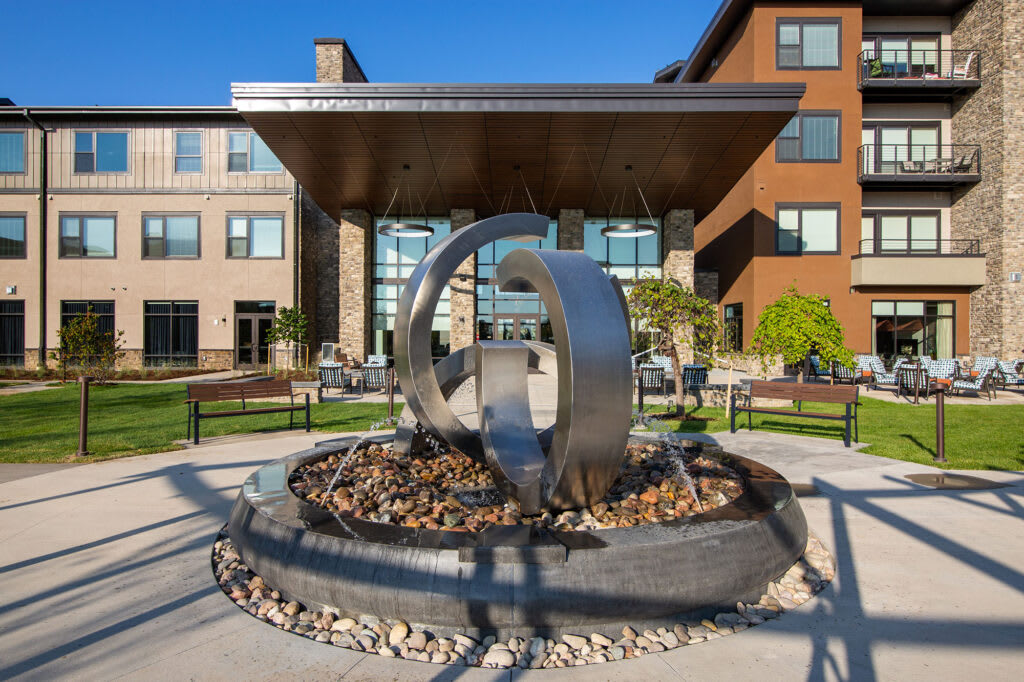 A modern building entrance featuring a circular metal sculpture surrounded by landscaped rocks.