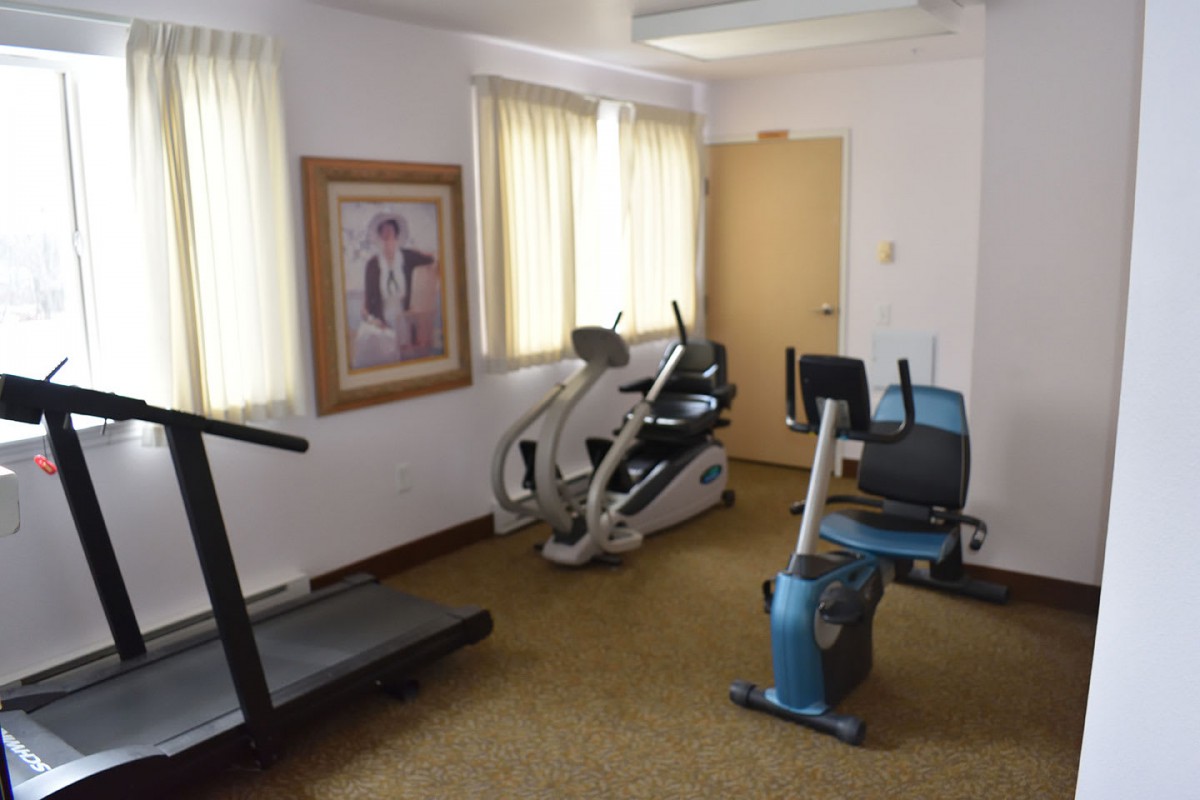 A small gym room with exercise equipment including a treadmill and stationary bikes.