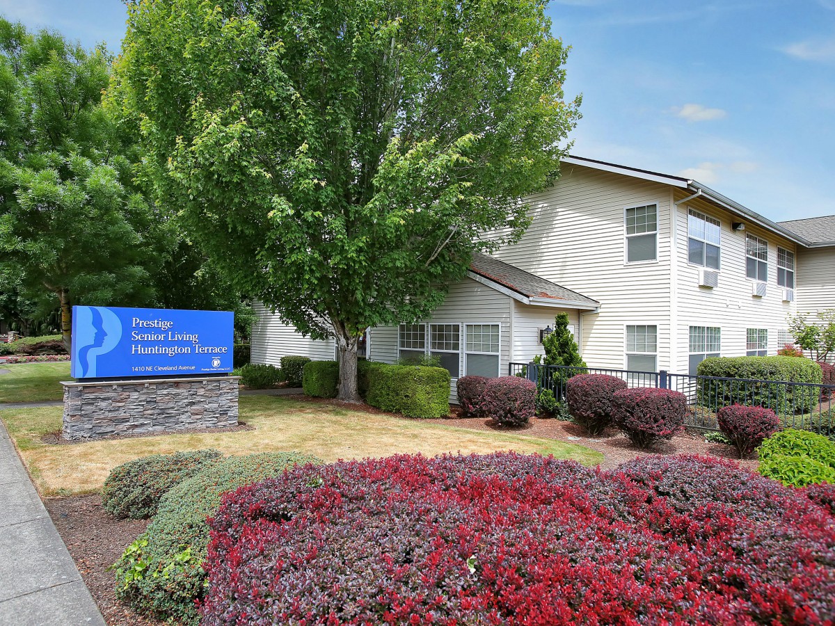 An apartment complex with well-maintained landscaping and a prominent sign in front.