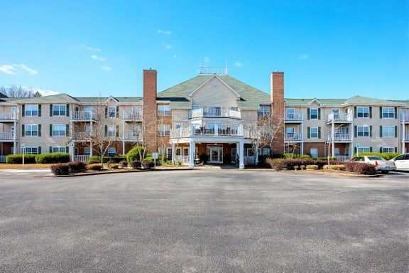 A large hotel building with a grand entrance and ample parking space under a clear blue sky.
