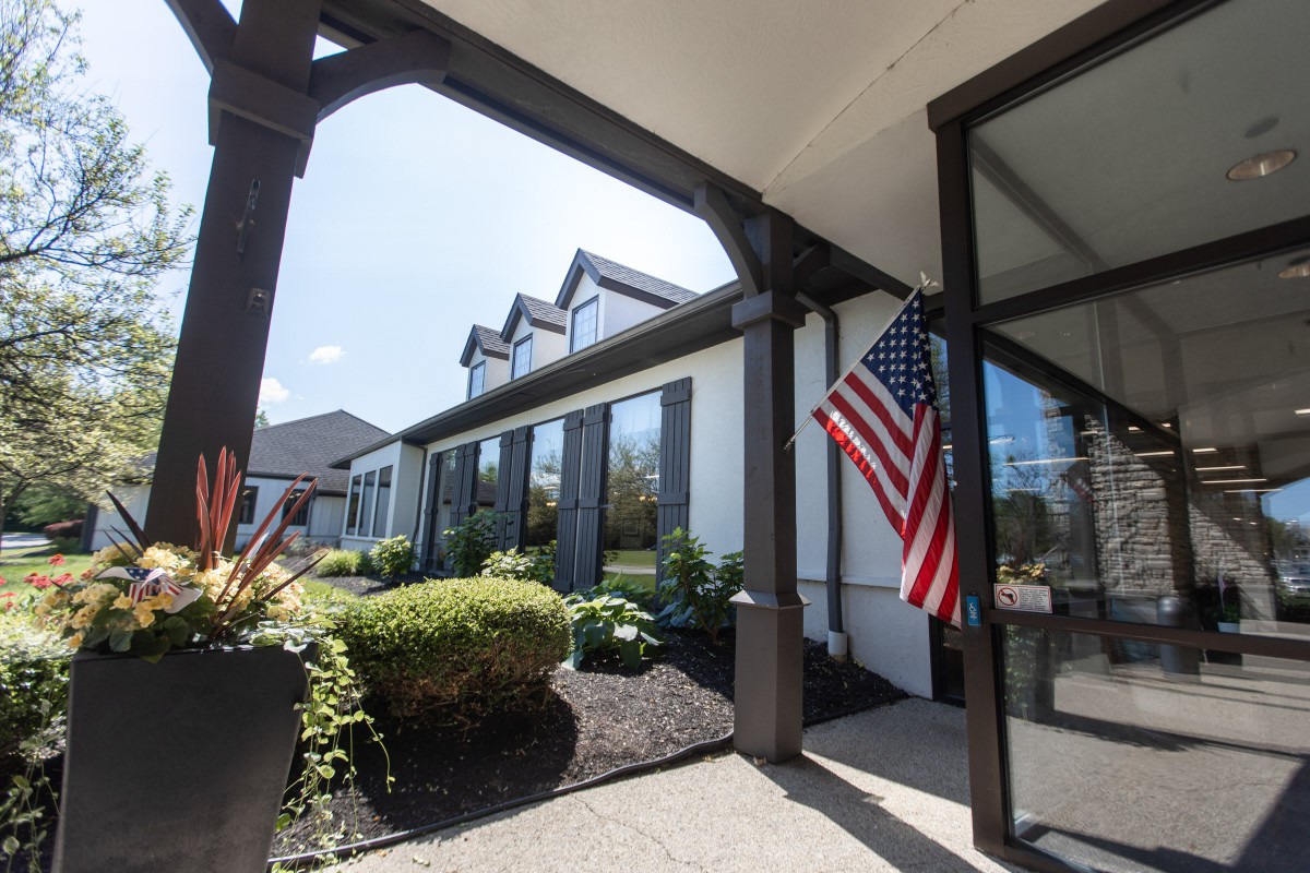 A modern house with a landscaped garden and an American flag displayed at the entrance on a sunny day.