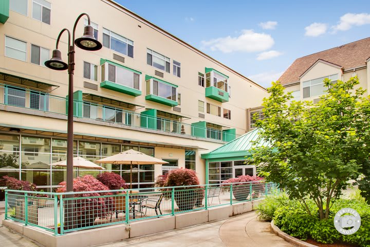 A modern apartment building with green accents and outdoor seating under patio umbrellas.
