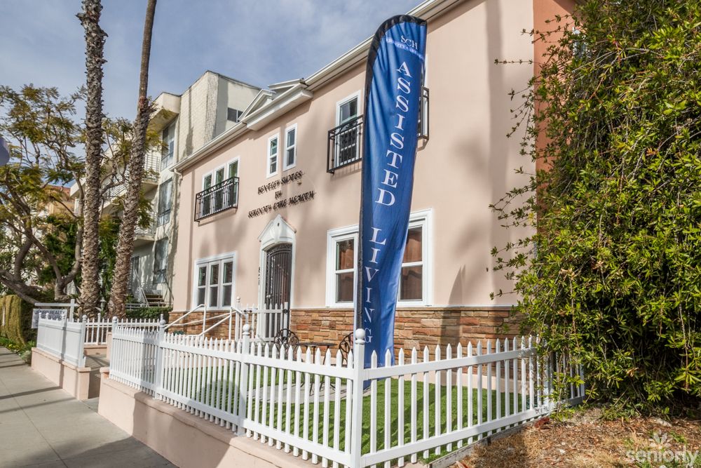 A residential building with a sign indicating 'Assisted Living' and a white picket fence in front.
