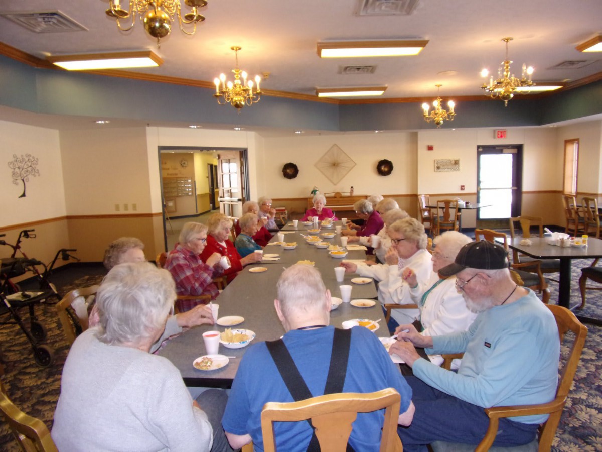 A group of seniors gathered around a dining table in a community setting.