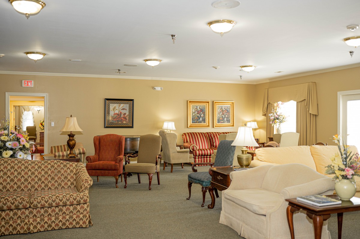 A cozy living room with a variety of chairs, sofas, artwork on the walls, and warm lighting.