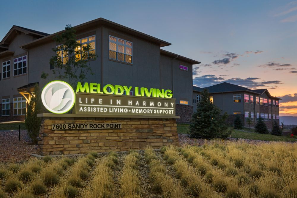 A view of the Melody Living assisted living facility with illuminated signage at dusk.